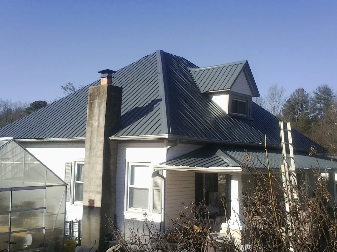 Dark blue standing seam metal roof on a white farmhouse with dormer — Slate & Tile Roof Repair by Roofing Brothers in Hillpoint