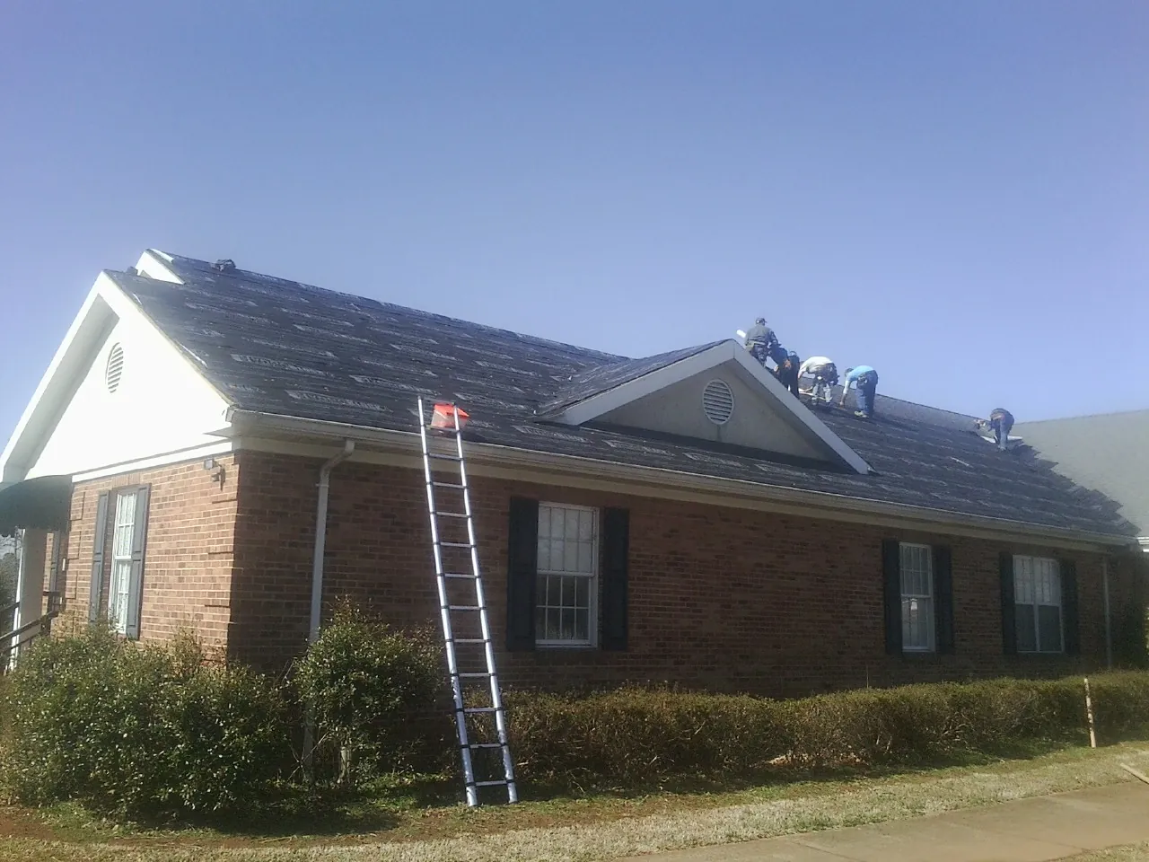 Crew tearing shingles off a brick ranch roof with a ladder set — Metal Roof Repair work by our crew in Hillpoint