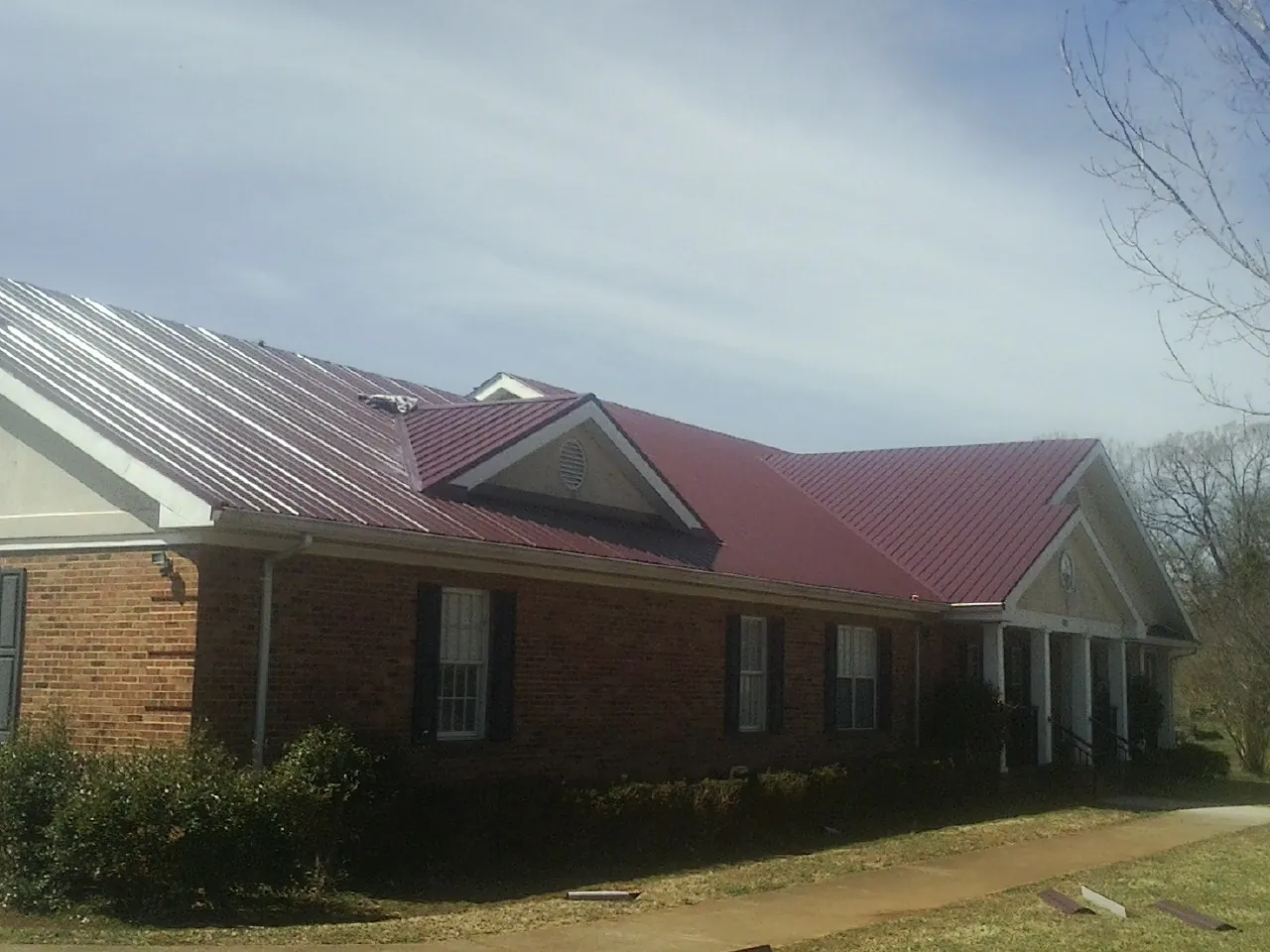 Red metal roof with gabled entries on a long brick building, from a Hail Damage Roof Repair job in Hillpoint