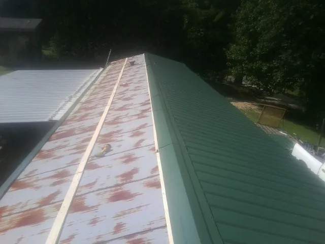 Old rusted panels beside newly installed green metal roofing — Wind Damage Roof Repair by Roofing Brothers in Hillpoint