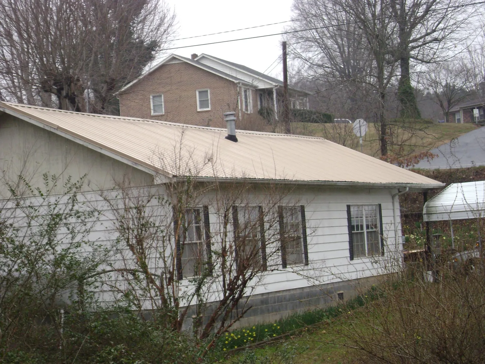 Tan metal roof on a white sided house set into a hillside — Commercial Roofing by Roofing Brothers in Hillpoint